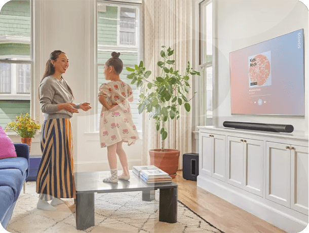 Family enjoying TV in bright living room with wall-mounted screen and soundbar audio system. 